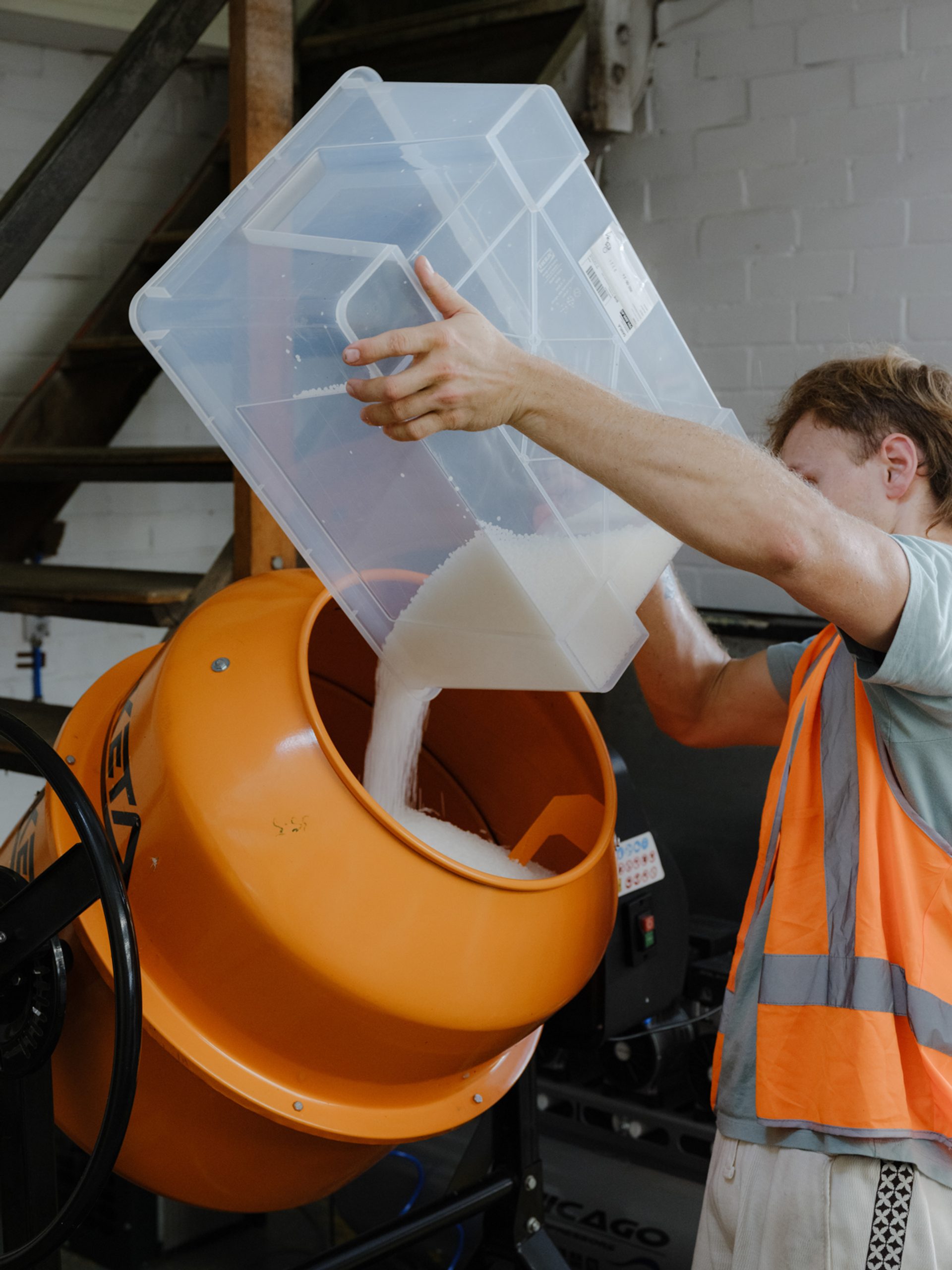 Figure pours plastic bits into a rotating mixer.