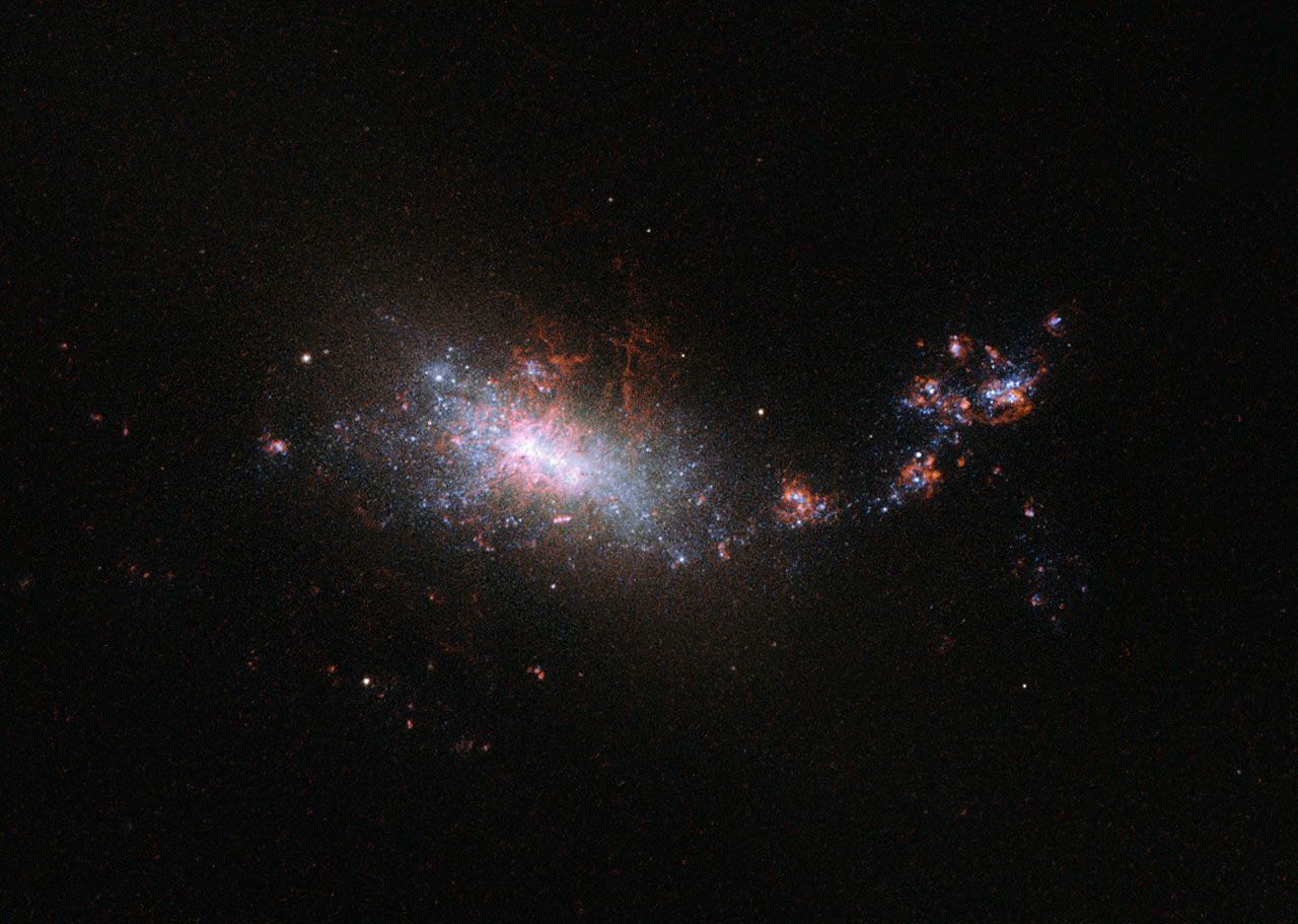 A dramatic telescope image of the galaxy NGC 1140, with an irregular form of bright white, blue and red starburst.