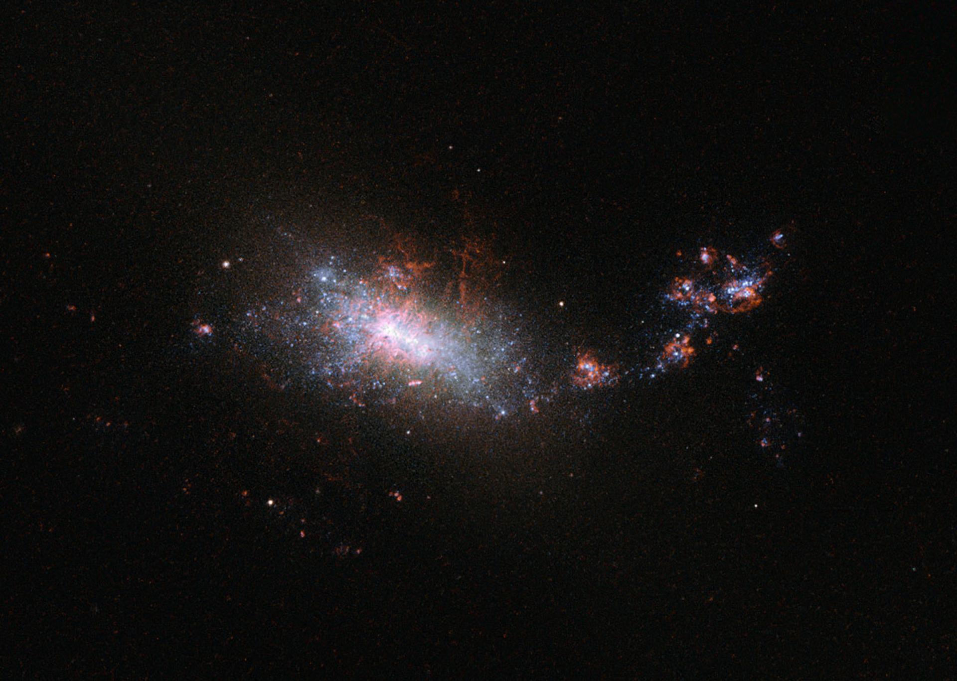 A dramatic telescope image of the galaxy NGC 1140, with an irregular form of bright white, blue and red starburst.