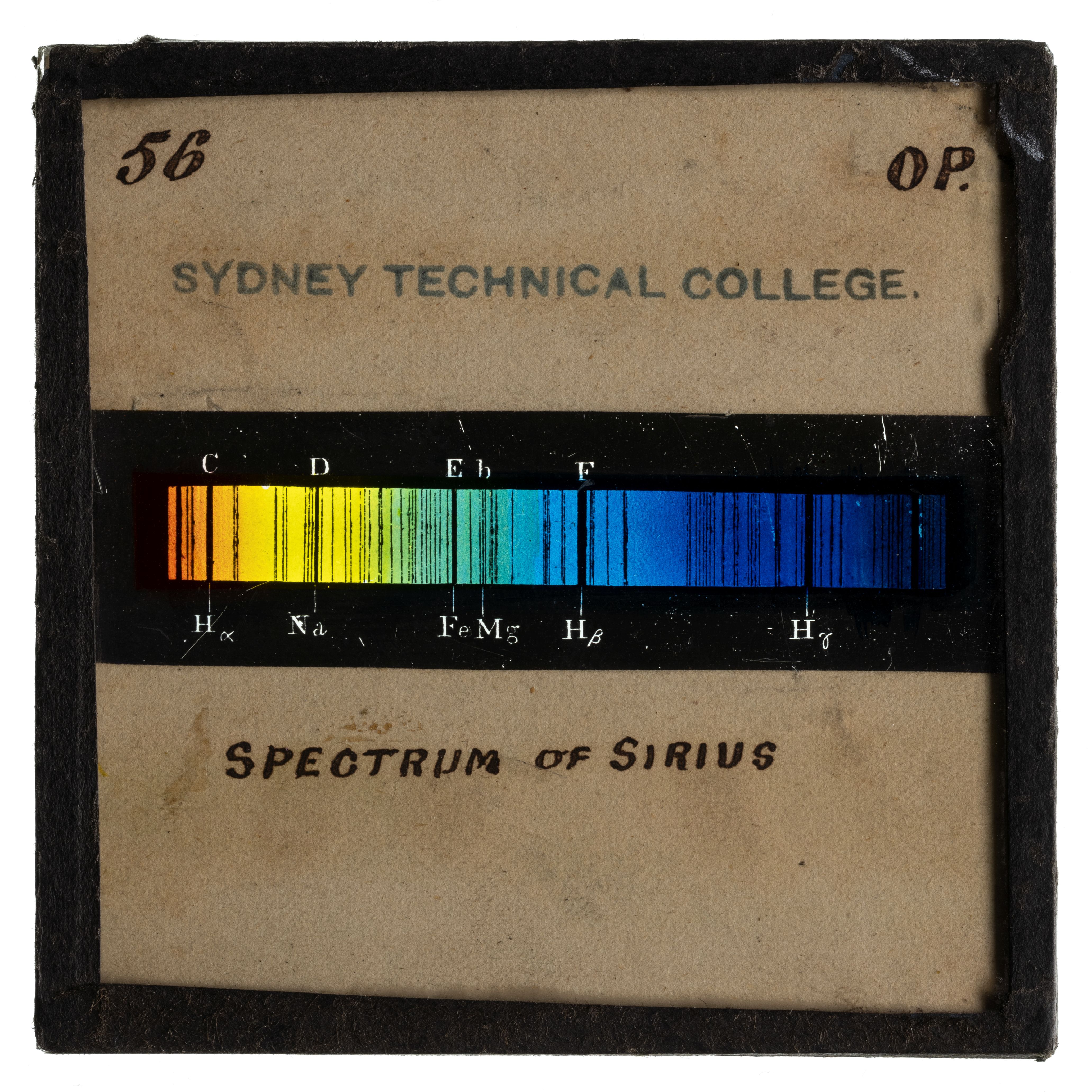 Photograph of a glass plate slide with a black frame and an image showing the spectrum of Sirius using a rainbow coloured bar with black line markings through out the bar.