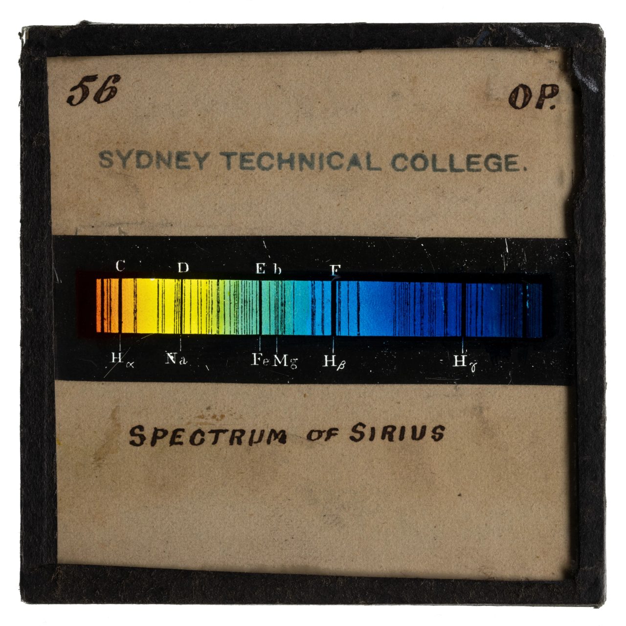 Photograph of a glass plate slide with a black frame and an image showing the spectrum of Sirius using a rainbow coloured bar with black line markings through out the bar.