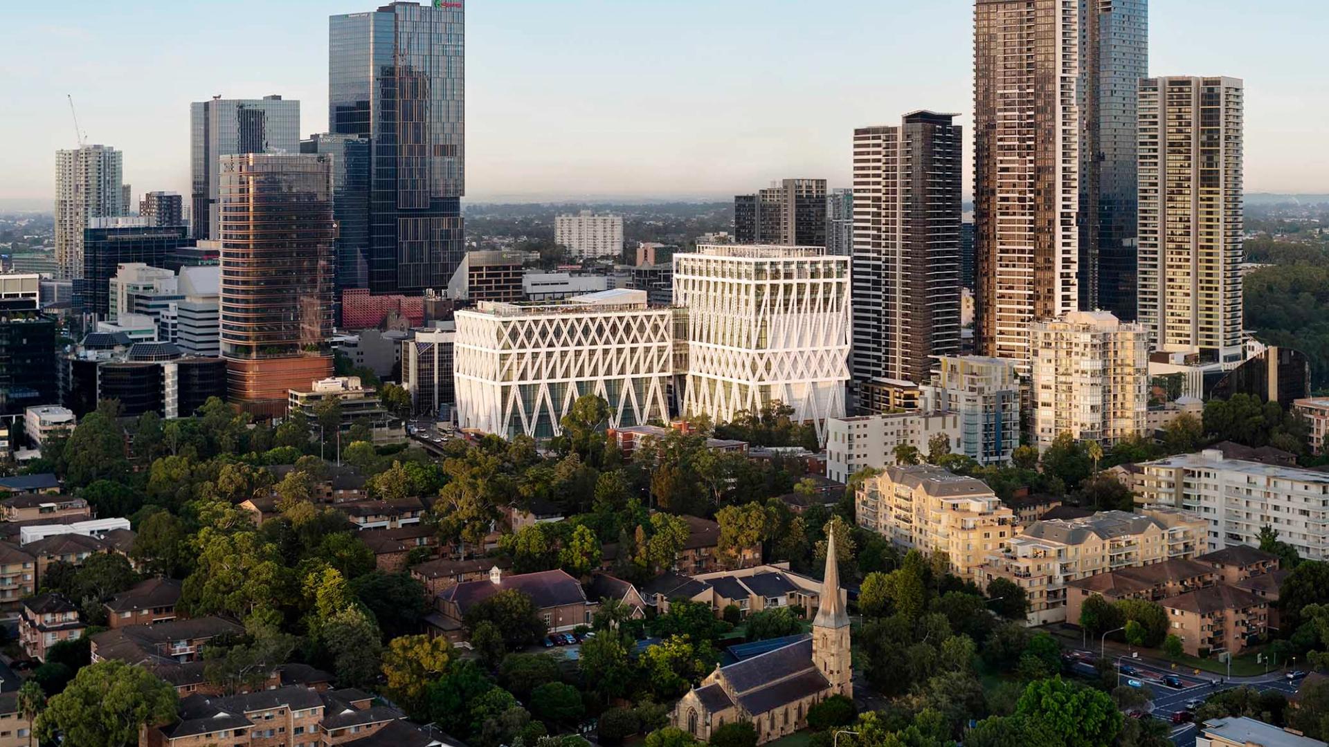 Aerial image of a suburban city, focusing on a building (Powerhouse Parramatta) with large white beams as an exterior exoskeleton in the centre.
