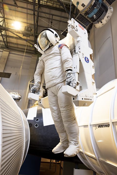 Figure suspended from ceiling wearing white spacesuit and machine.