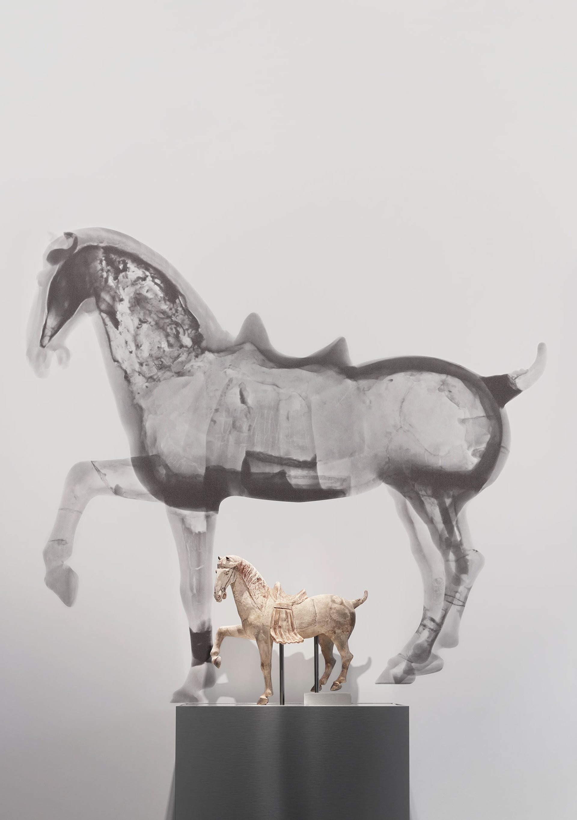 Small horse figure on a plinth in front of a large black and white neutron tomography scan of the same horse figure.
