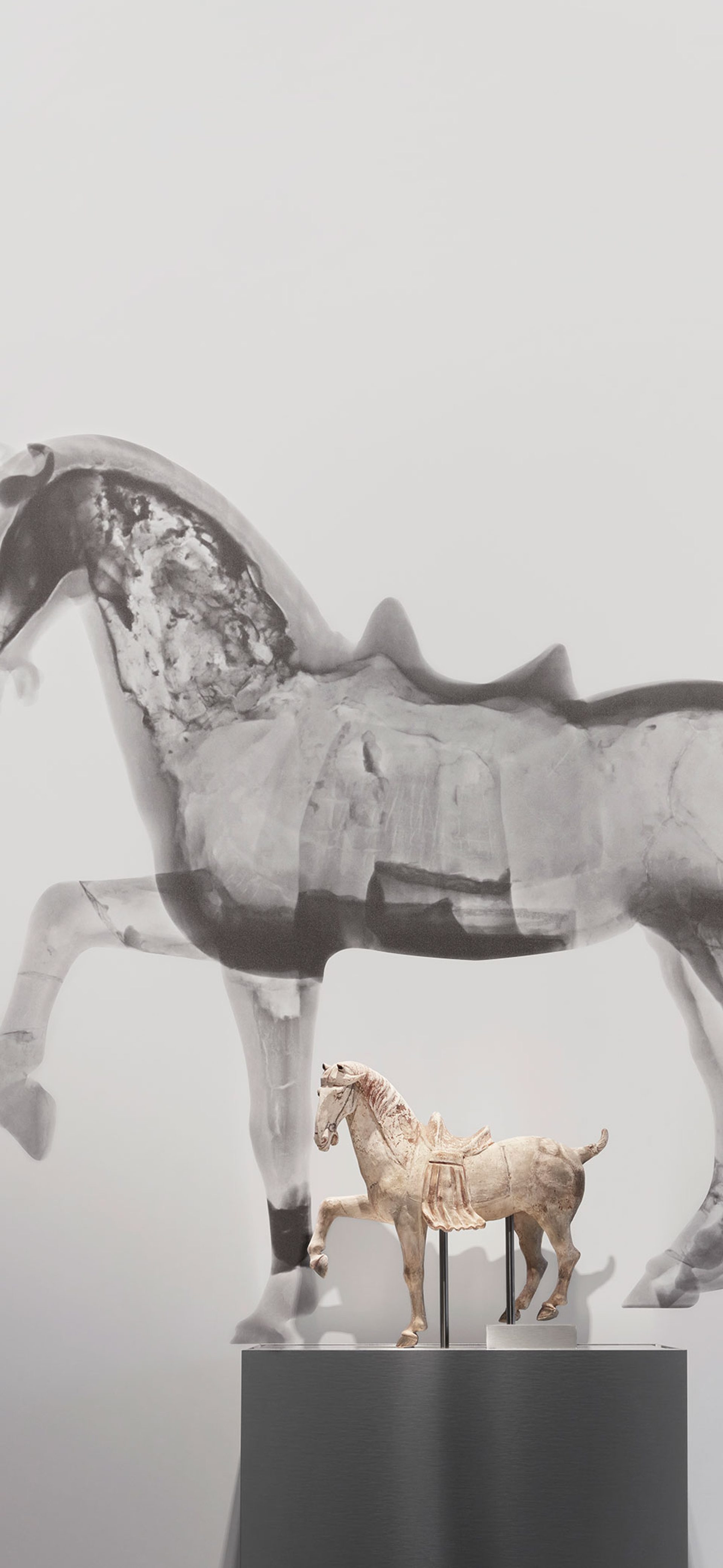 Small horse figure on a plinth in front of a large black and white neutron tomography scan of the same horse figure.