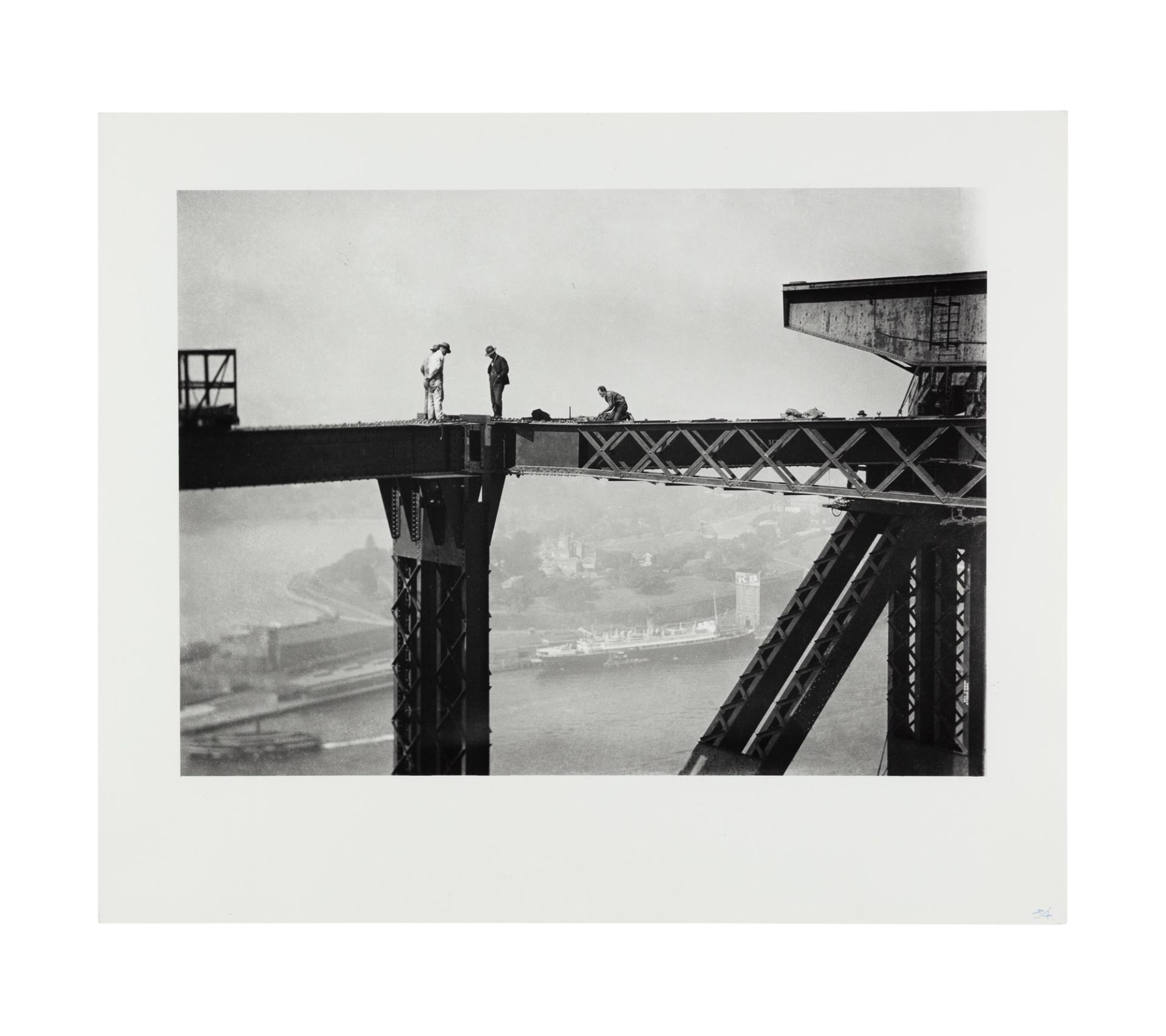 Image of three figures standing on the top of the harbour bridge. A fourth figure is crouched further along the bridge girder to their right. In the background, the harbour is visible below.