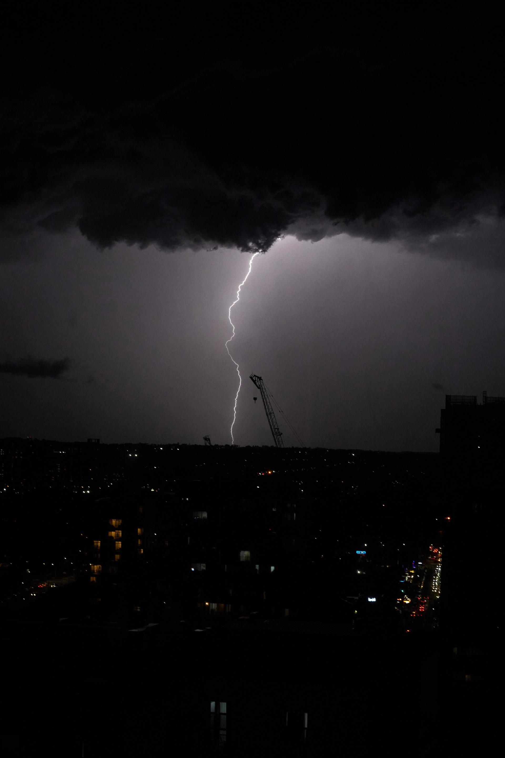 Lightening strikes the horizon line atop a city at night.