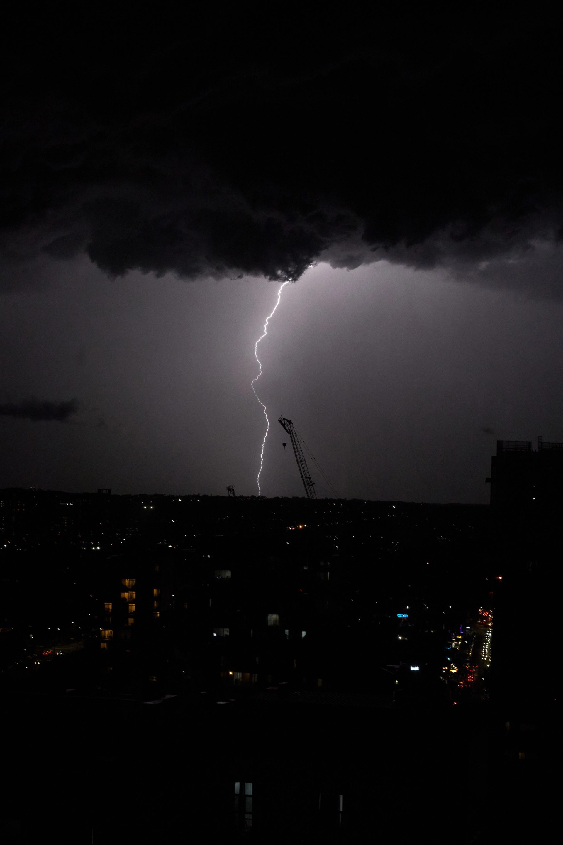 Lightening strikes the horizon line atop a city at night.