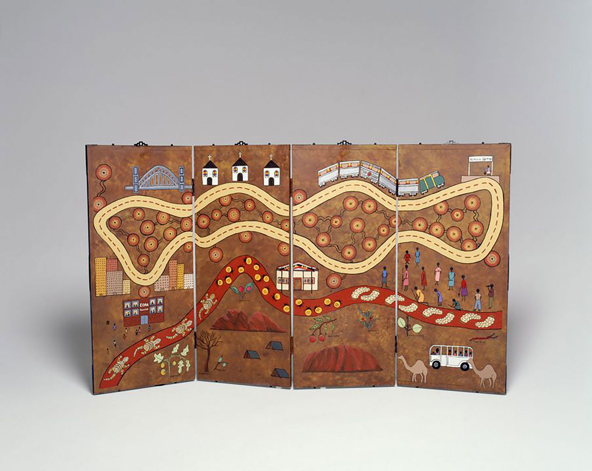 Landscape orientation mural with four vertical panels hinged together. On each corner and on both vertical ends are metal plates with impressed floral designs. Spaced along the horizontal ends are metal studs. At the top are ornate picture hooks painted in black acrylic paint. The image on the front is multicoloured, in acrylic paint. Depicted in the top half is a continuous oval road around which are a bridge, churches, a train and carriages marked 'Australian National / THE GHAN', and a figure standing under a sign marked 'Alice Springs'. The lower half is bisected by an ochre coloured road decorated with lizards and insects. Above this road, are buildings marked 'Eora Centre' with figures, and 'Legal Aid'. On the far right is a group of figures, some with sticks. Below the ochre road are plants with names written next to them, including 'BUSH TOMATO', 'MULGA TREE', 'QUANDONG' and 'MISTLETOE'. Interspersed with these are Uluru, tents, camels and a bus with people on it.