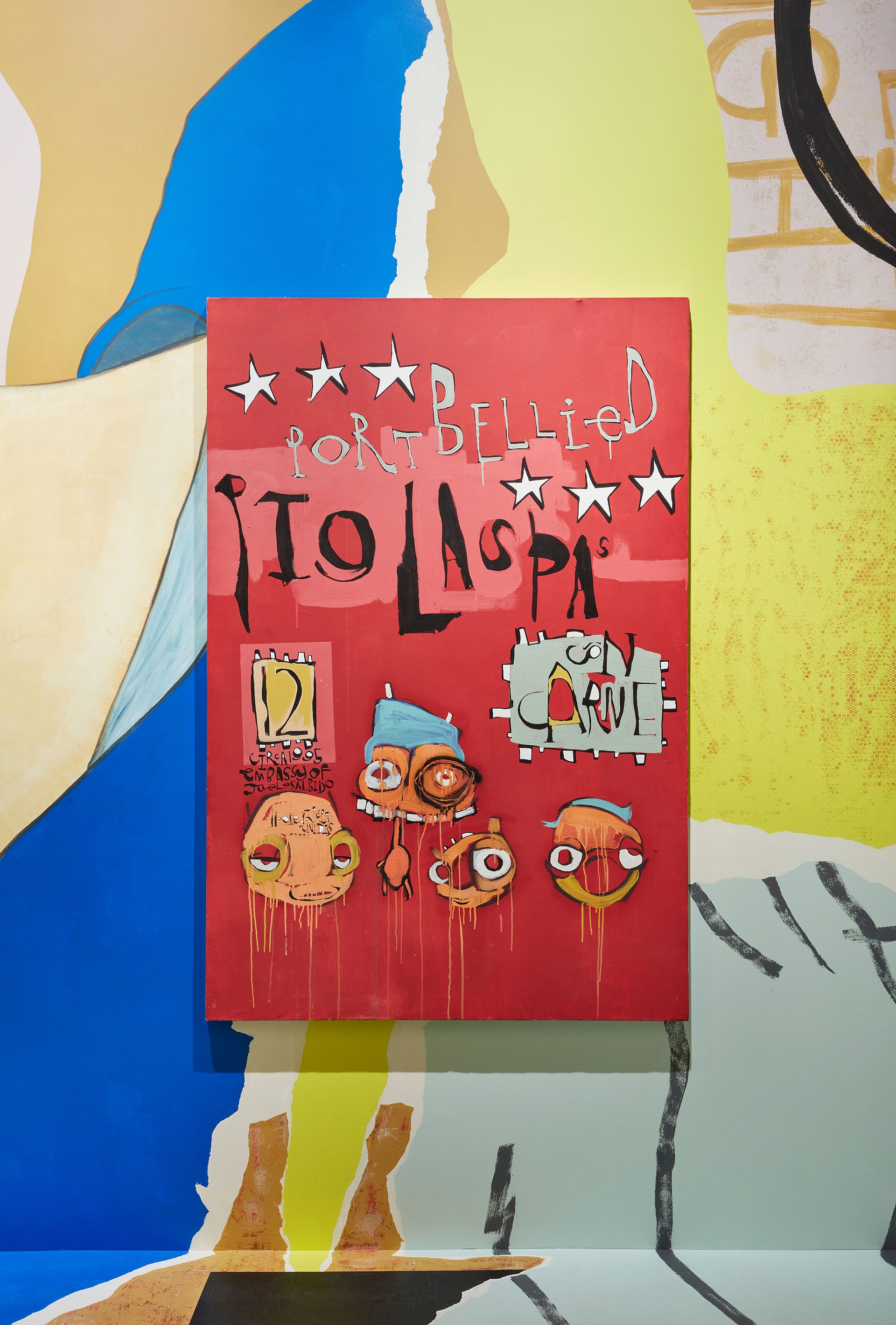 A brightly coloured wall of orange, blue and yellow. There is a mounted canvas on in it with a red background and paintings of five nonhuman characters.