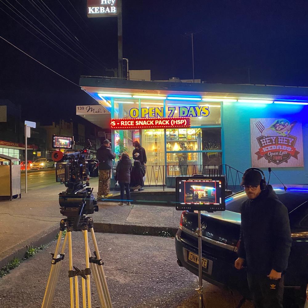 A film crew is outside a kebab shop at night.
