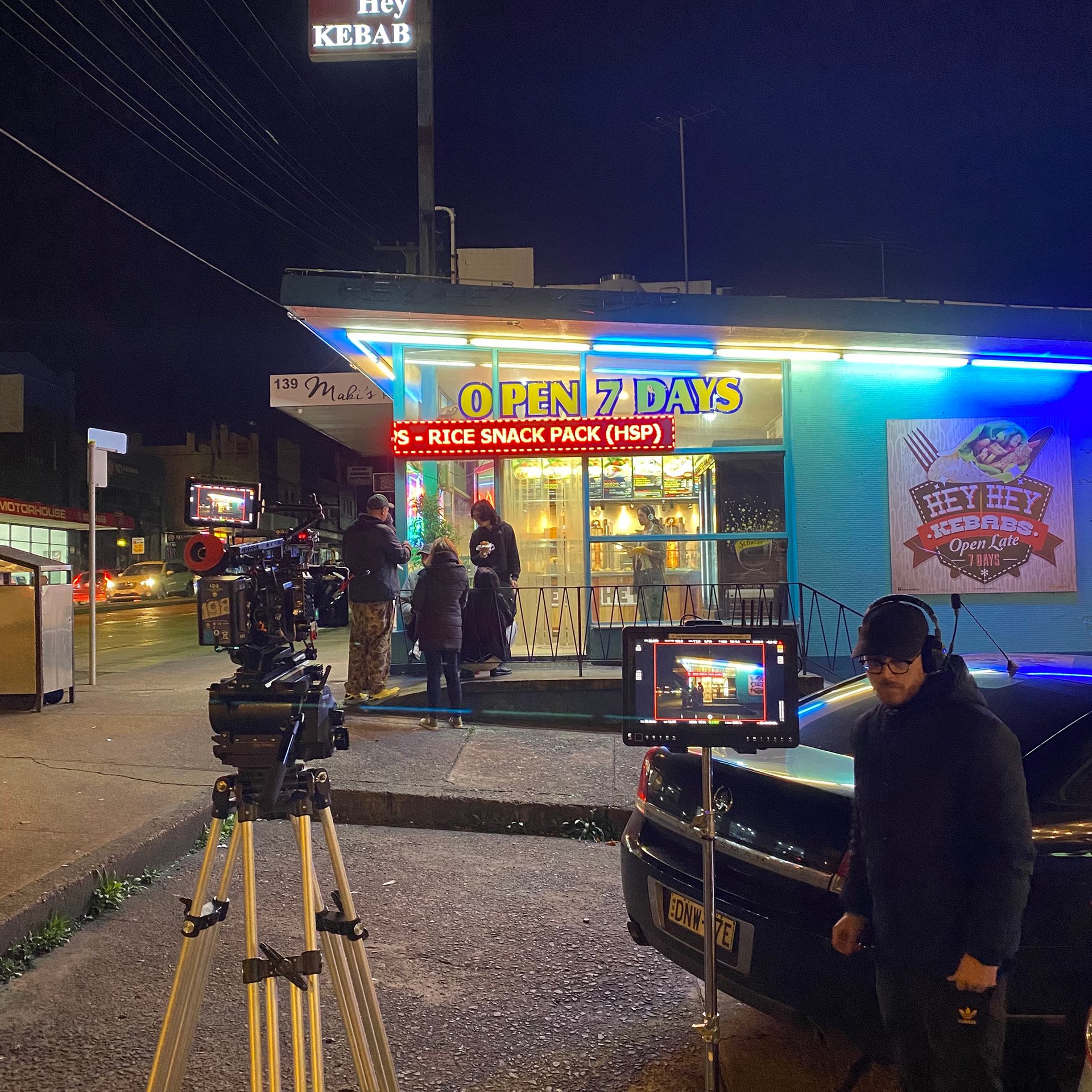 A film crew is outside a kebab shop at night.
