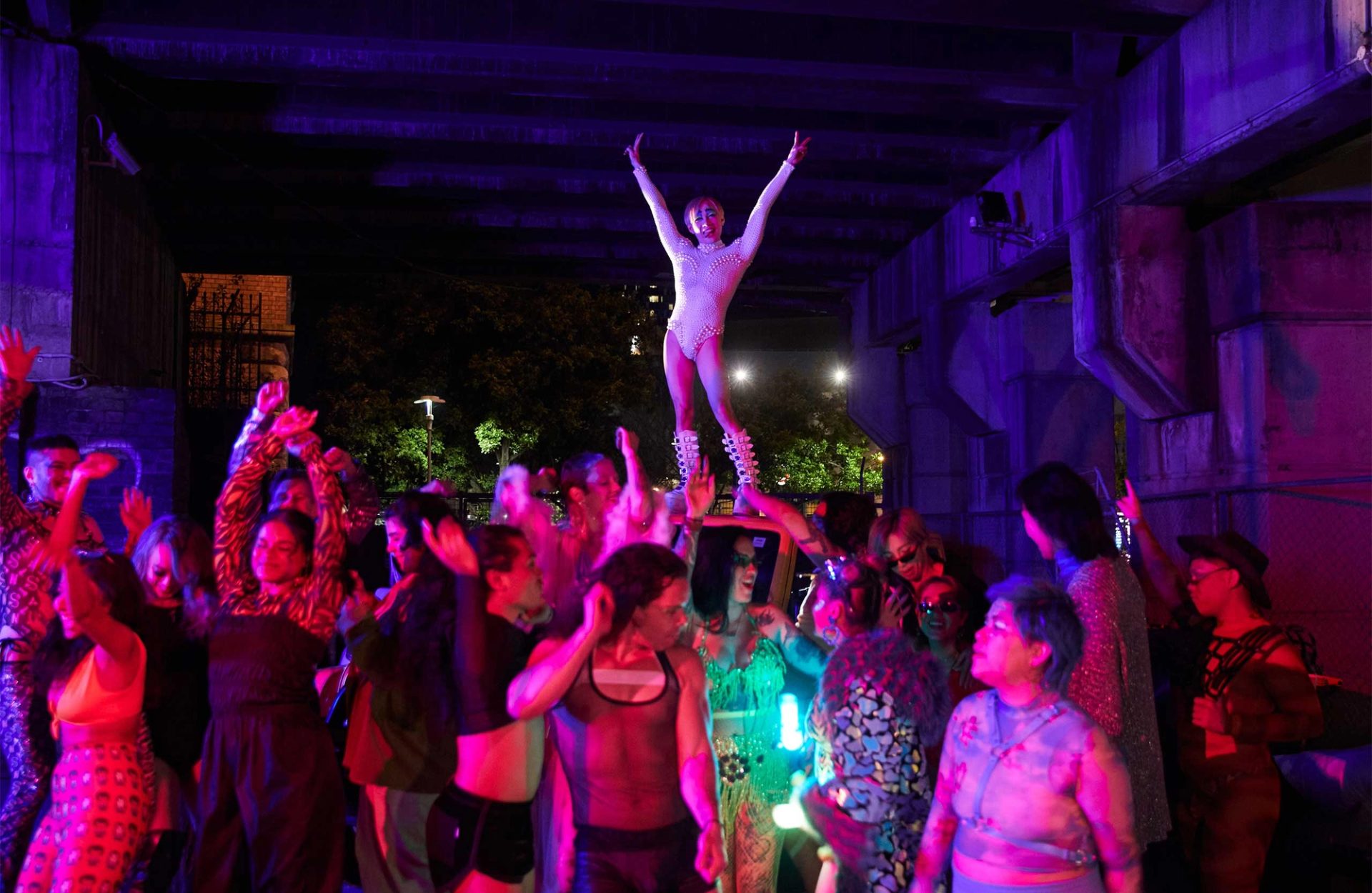 People dancing in a purple light, with figure posing above them all