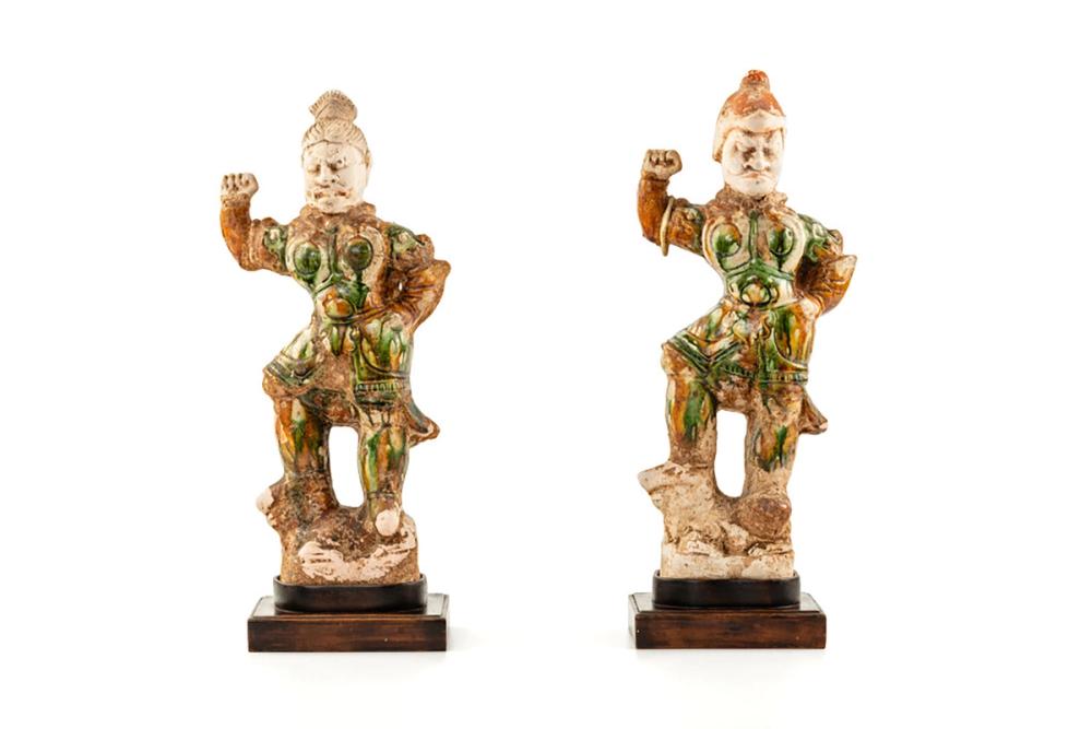 Two small ceramic warrior figures stand with one fist raised and are painted with green and orange.