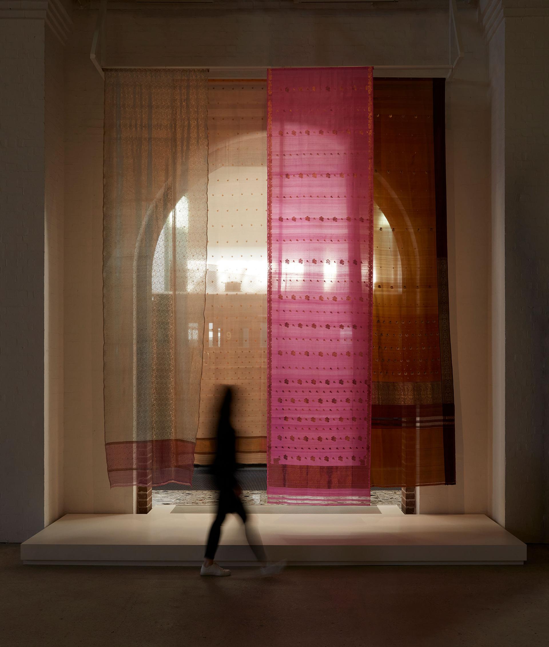 A figure walks in front of four floor to ceiling length fabric