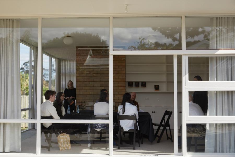 People sitting within a room with glass walls and brick