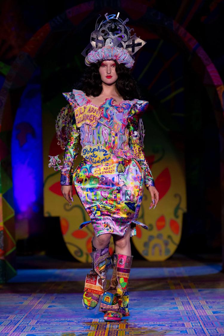 Runway model wearing a structured colourful dress with matching boots and matching headpiece.