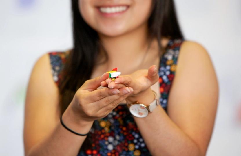 A Creative Studio participant wearing a colourful singlet and a watch holds up a small piece of Lego
