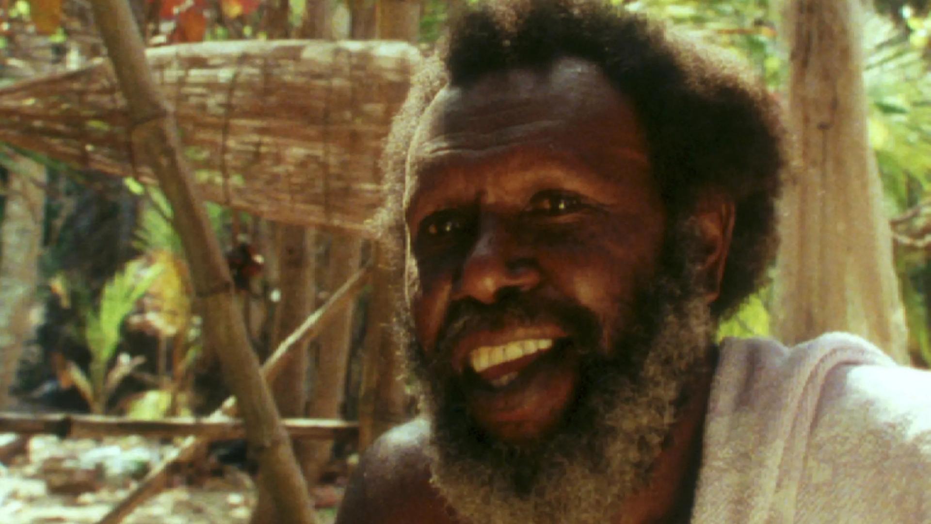 Koiki Mabo sitting within bamboo and sand backgorund.