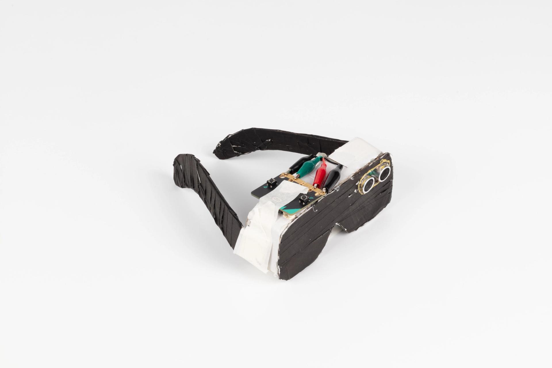 Image of a hand crafted mechanical device against a white background. Glasses made of cardboard with wires and cameras attached to the lens.