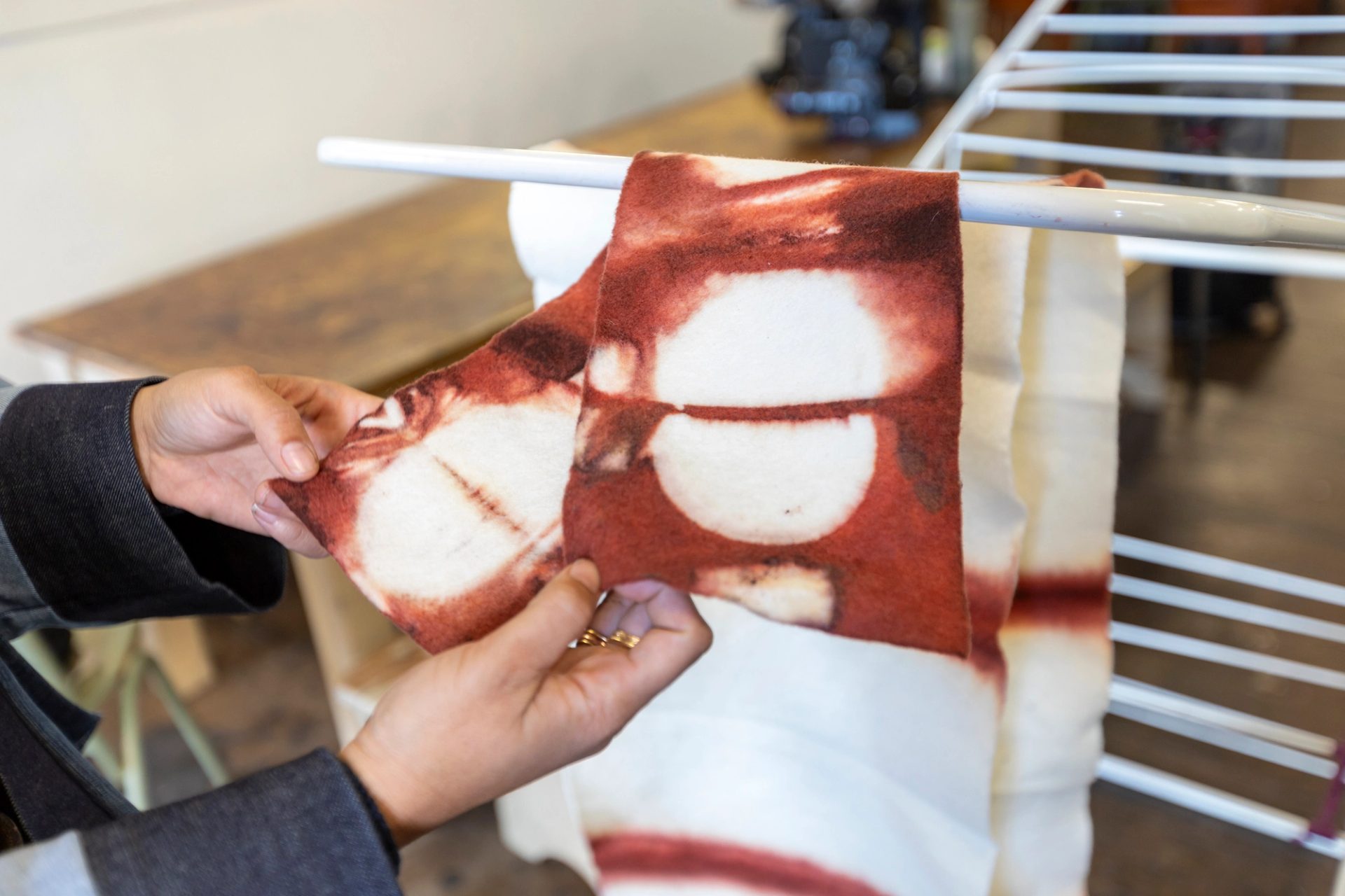Two hands holding a piece of textile, which is light cream,with naturally-dyed red patterns.