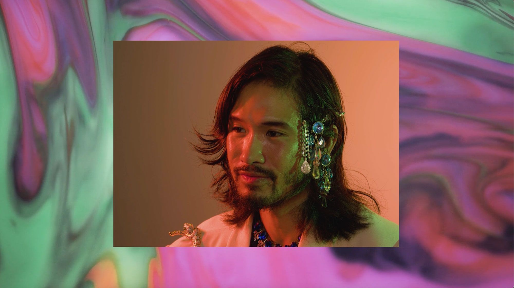 Paul Bui is in centre frame wearing a crystal headpiece. There is a multicoloured swirling background.