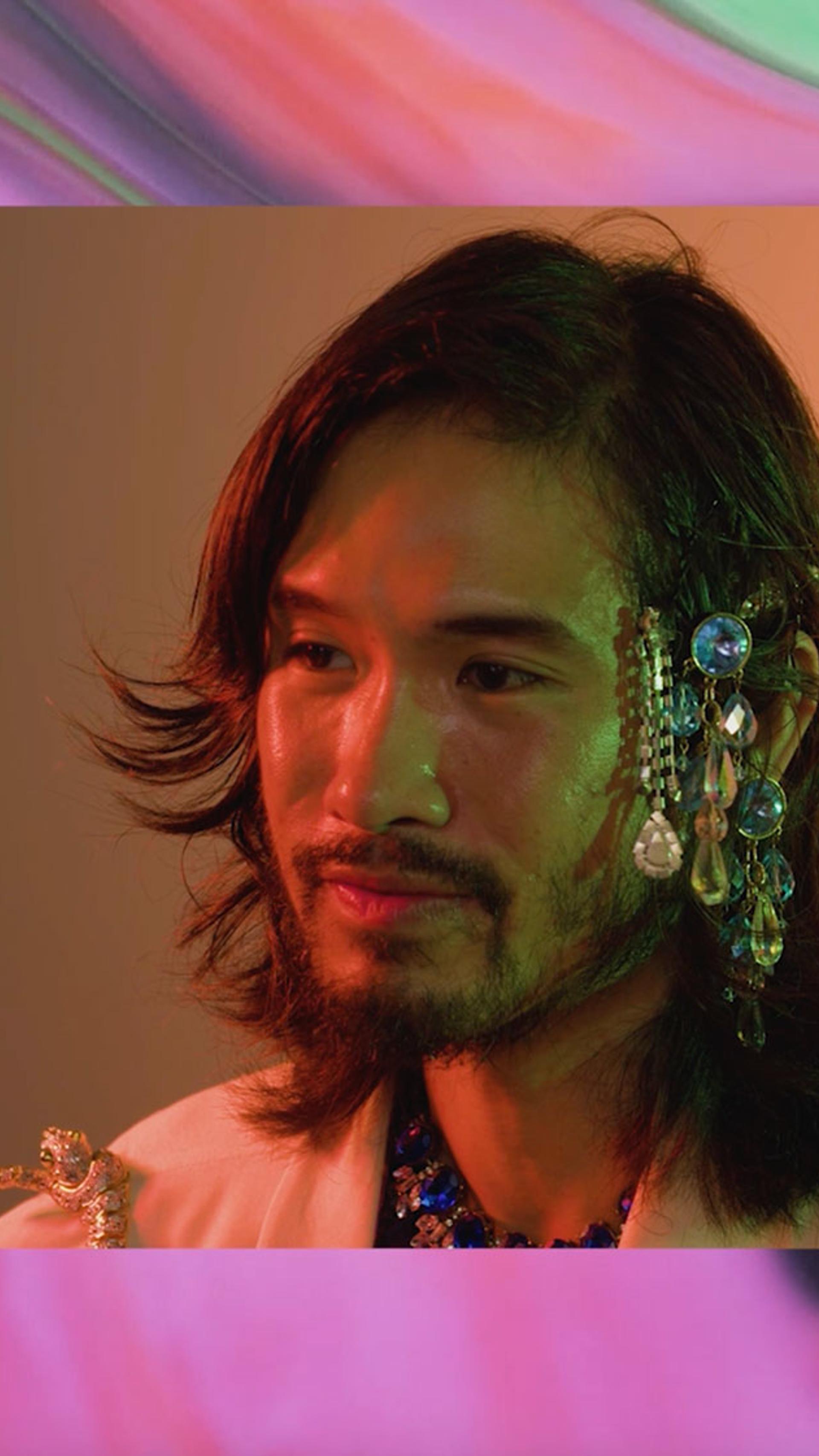 Paul Bui is in centre frame wearing a crystal headpiece. There is a multicoloured swirling background.