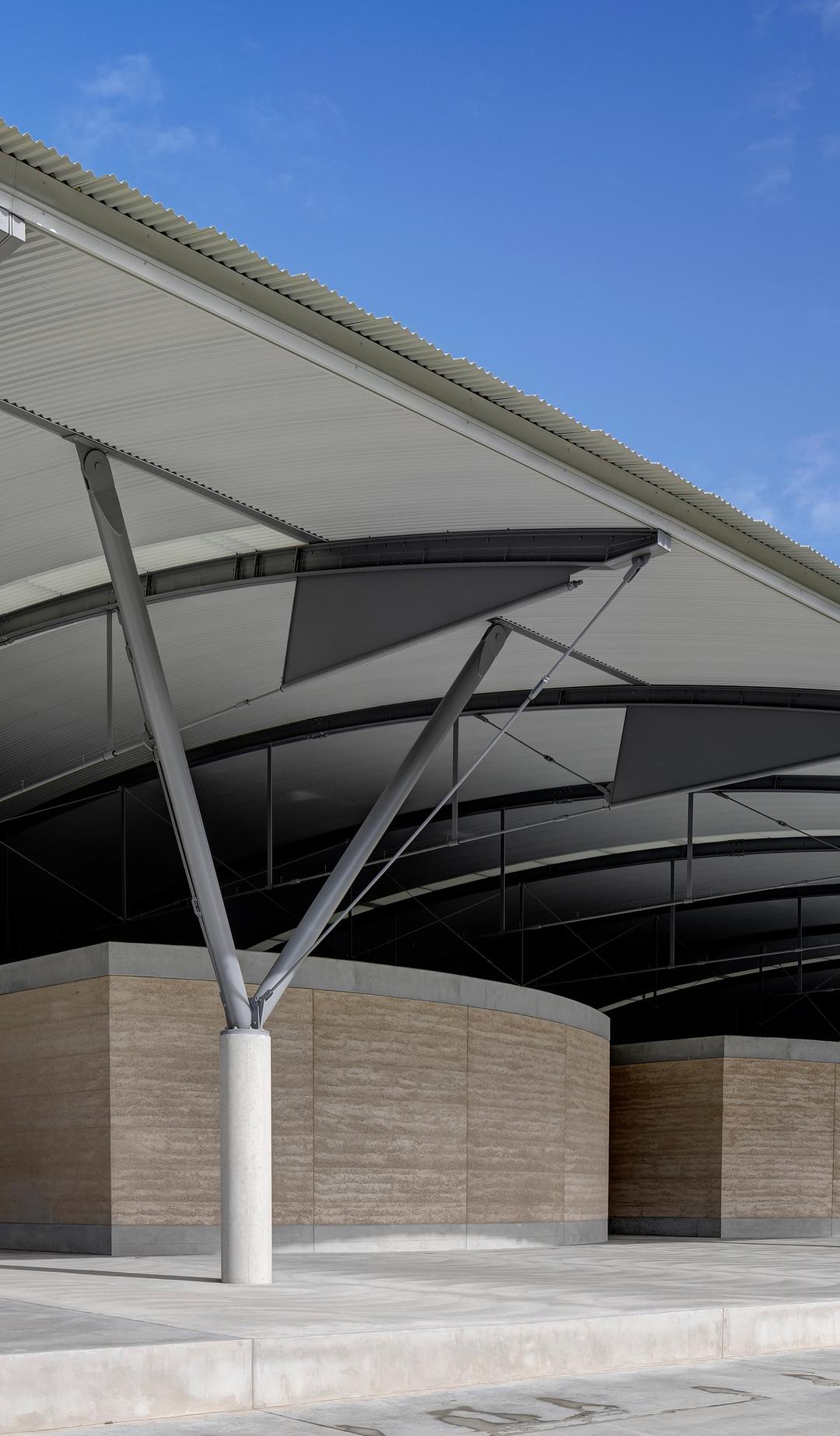 The interior steel structure of the National Herbarium’s roof above low stone walls, supported by a Y-shaped frame.