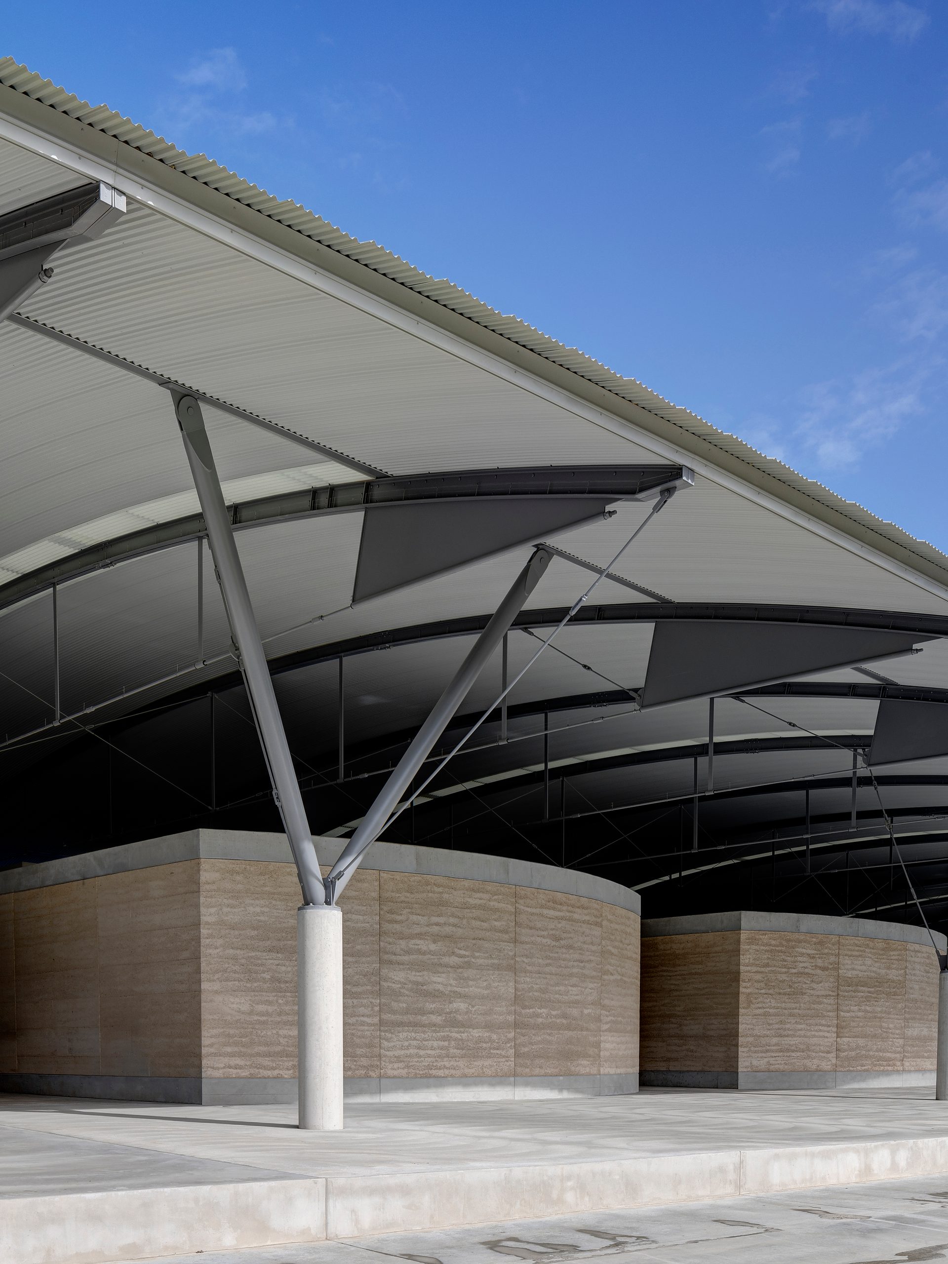 The interior steel structure of the National Herbarium’s roof above low stone walls, supported by a Y-shaped frame.