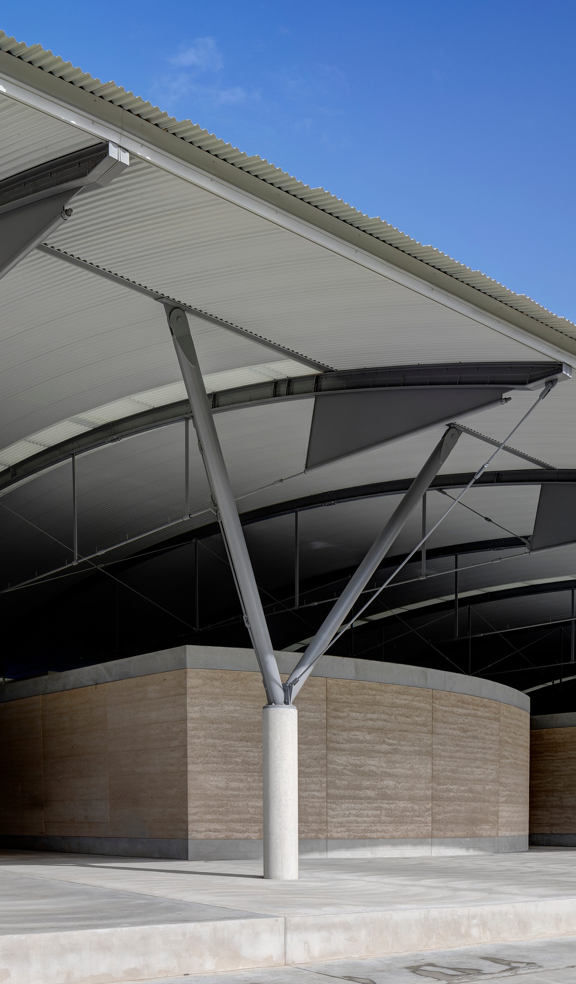 The interior steel structure of the National Herbarium’s roof above low stone walls, supported by a Y-shaped frame.