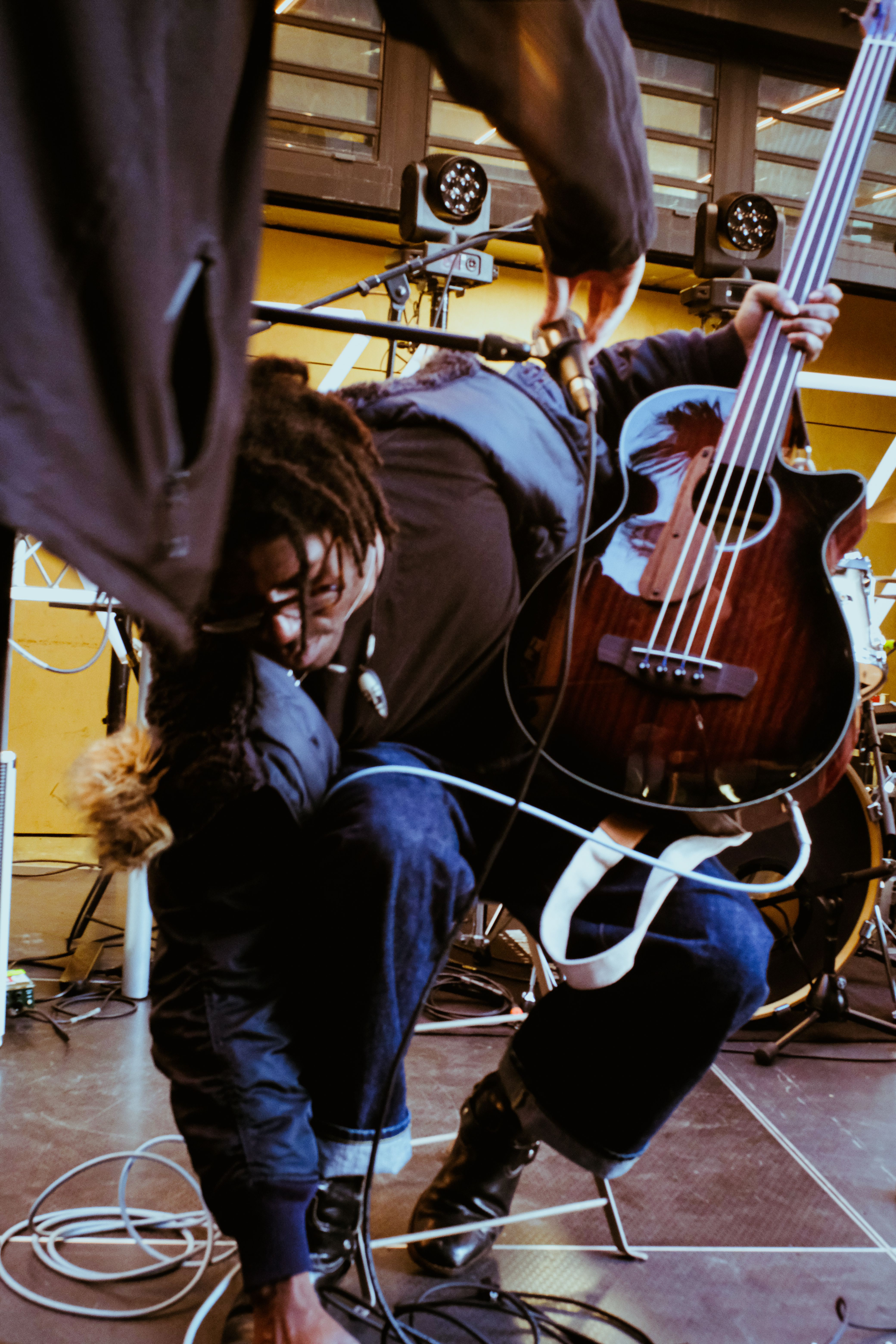 The performer FRIDAY* onstage at a street show in Parramatta. The photograph is a mid-shot, depicting FRIDAY* holding a guitar, plugging it into an amp.