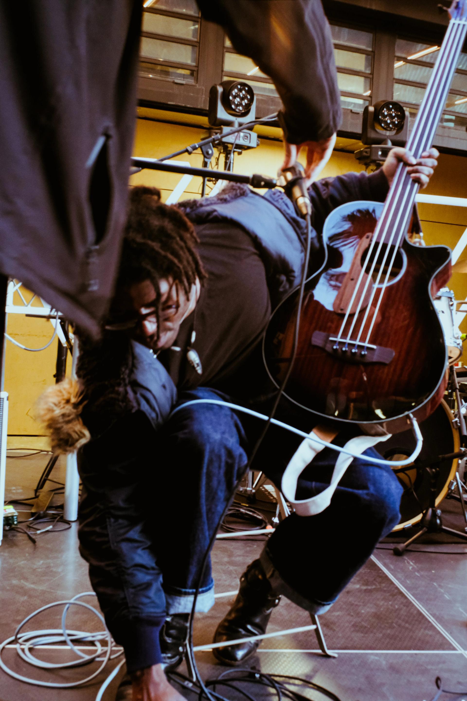 The performer FRIDAY* onstage at a street show in Parramatta. The photograph is a mid-shot, depicting FRIDAY* holding a guitar, plugging it into an amp.