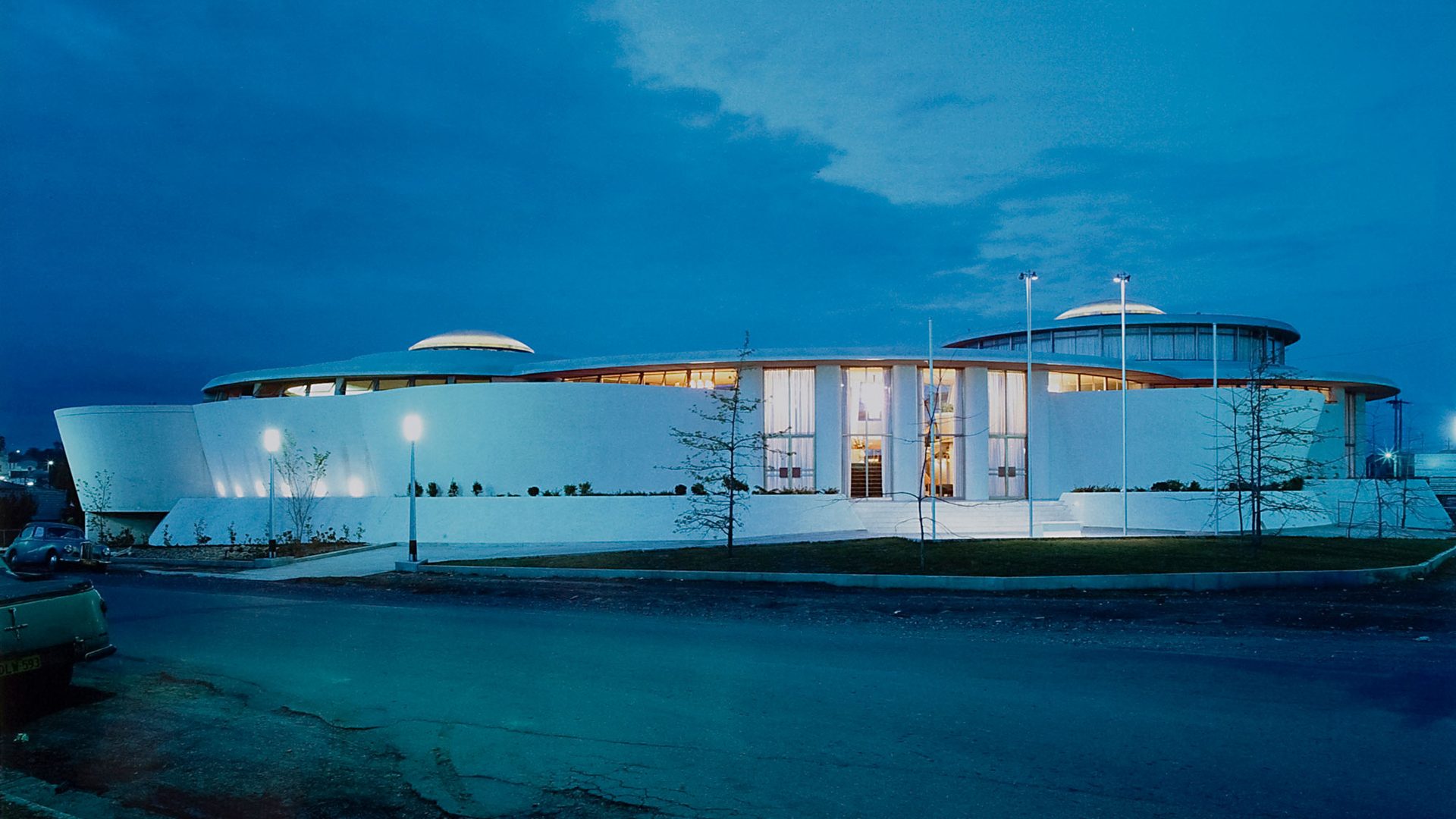 Gloss colour photographic print of the exterior of a white single level 1960s building, the Granville Returned Servicemen's Leagues Club photographed at night. The photograph has a small, embossed icon in the left hand corner with the text 'Max Dupain and Associates Archival Print'.