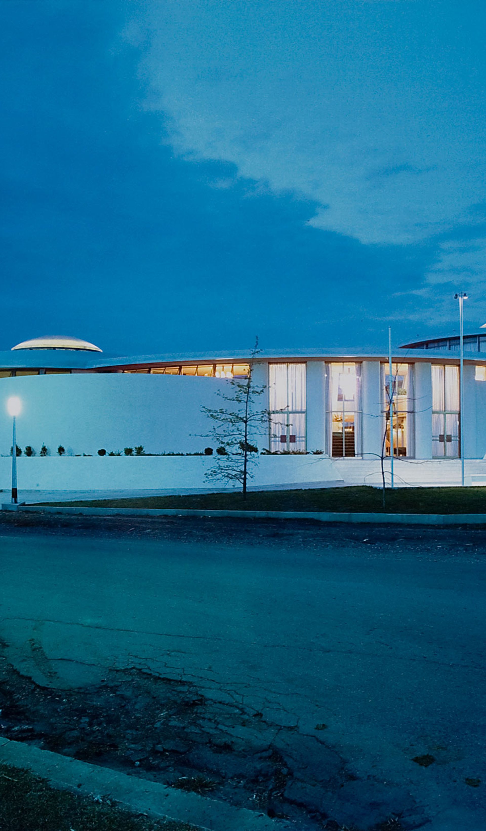 Gloss colour photographic print of the exterior of a white single level 1960s building, the Granville Returned Servicemen's Leagues Club photographed at night. The photograph has a small, embossed icon in the left hand corner with the text 'Max Dupain and Associates Archival Print'.