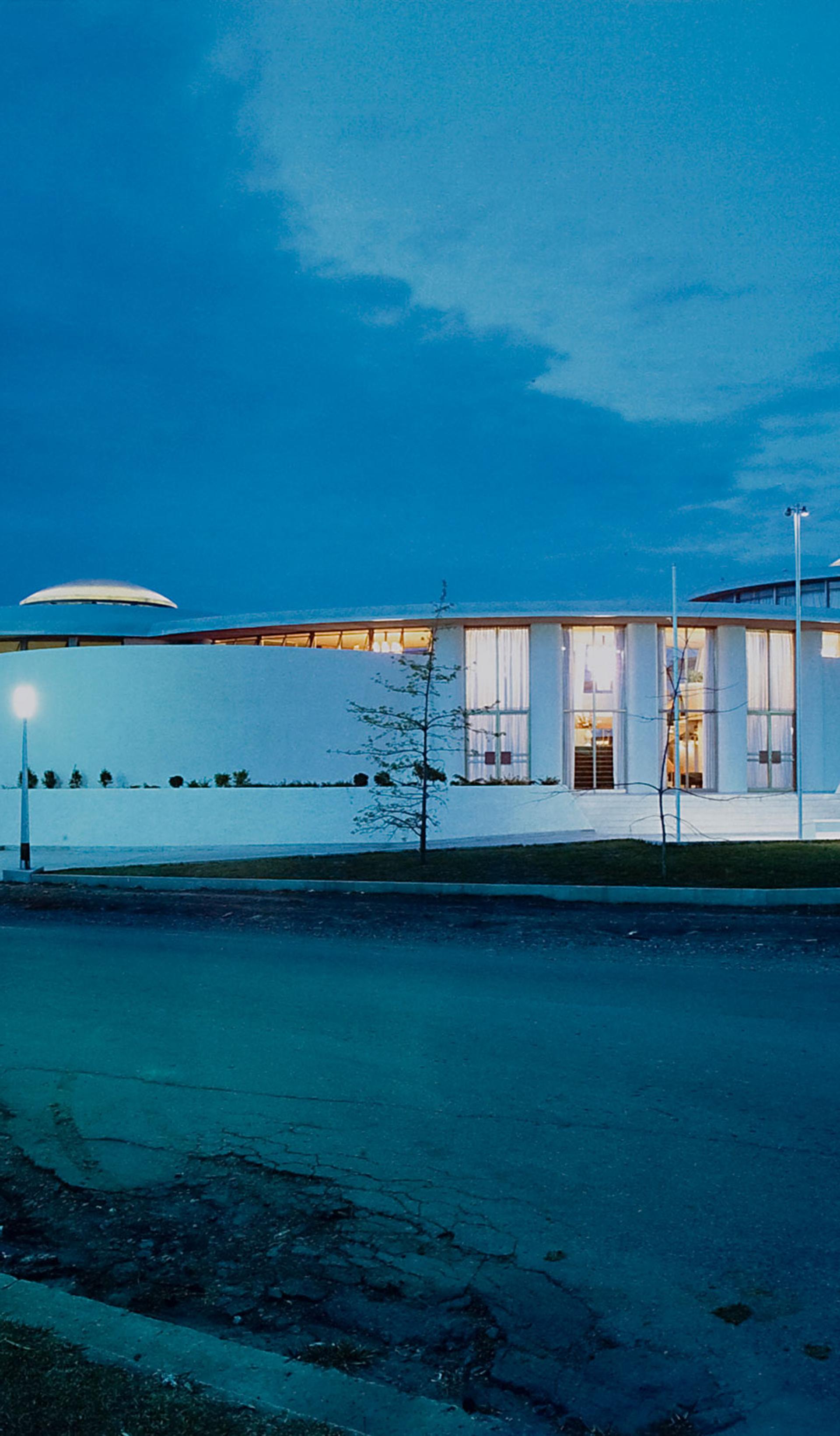 Gloss colour photographic print of the exterior of a white single level 1960s building, the Granville Returned Servicemen's Leagues Club photographed at night. The photograph has a small, embossed icon in the left hand corner with the text 'Max Dupain and Associates Archival Print'.