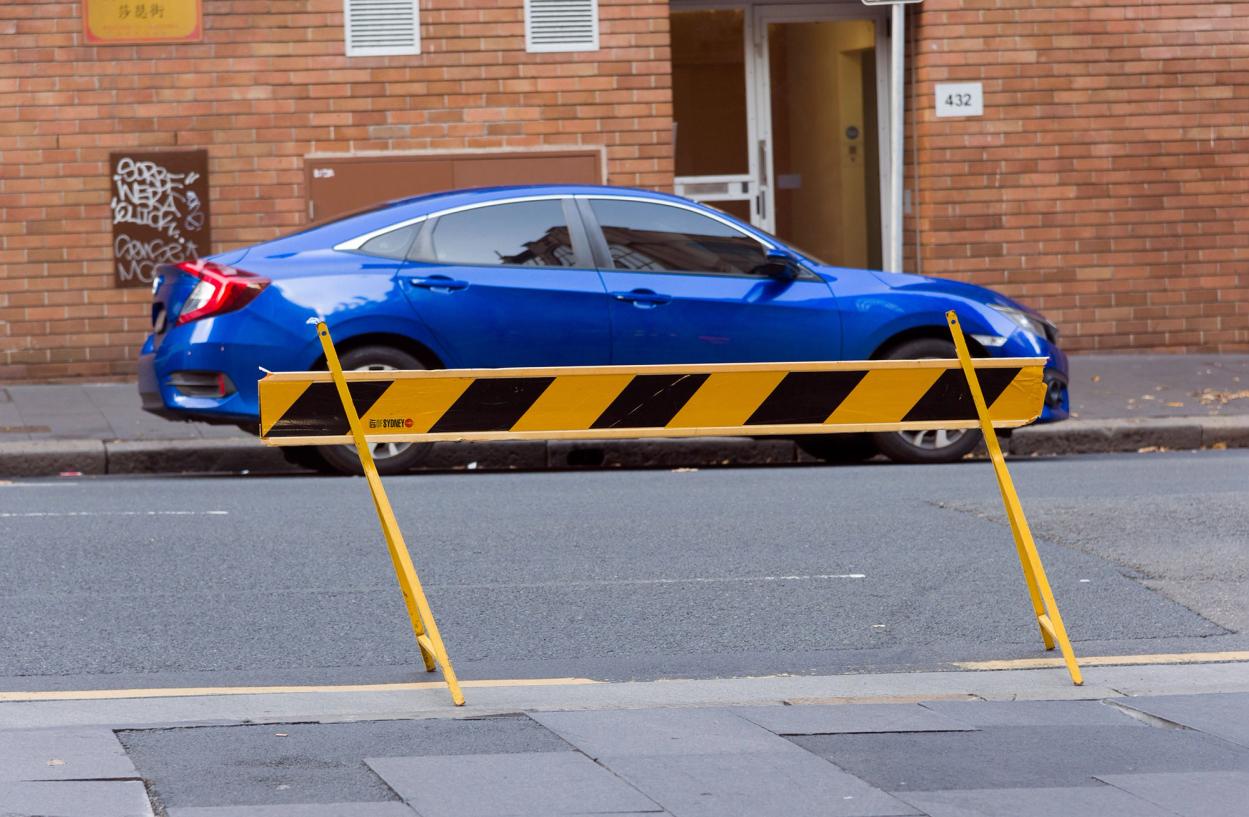 A blue car is parked on the side of the road, a yellow and black road barrier board is in the foreground.