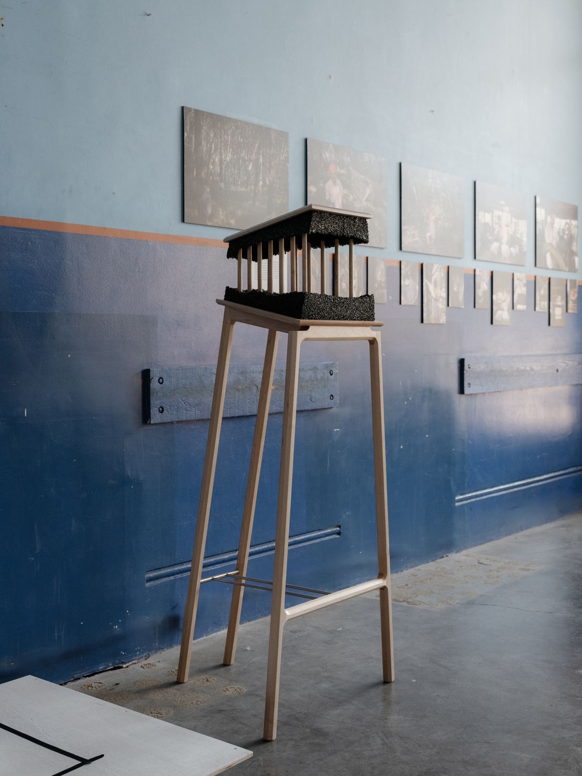 Tall legged table showcasing a 3d sculpture with photos on a wall in the background