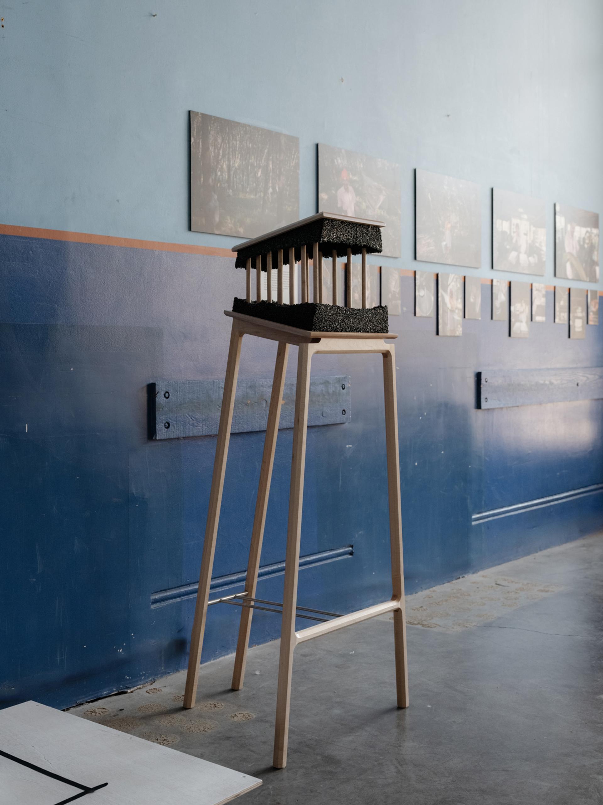 Tall legged table showcasing a 3d sculpture with photos on a wall in the background