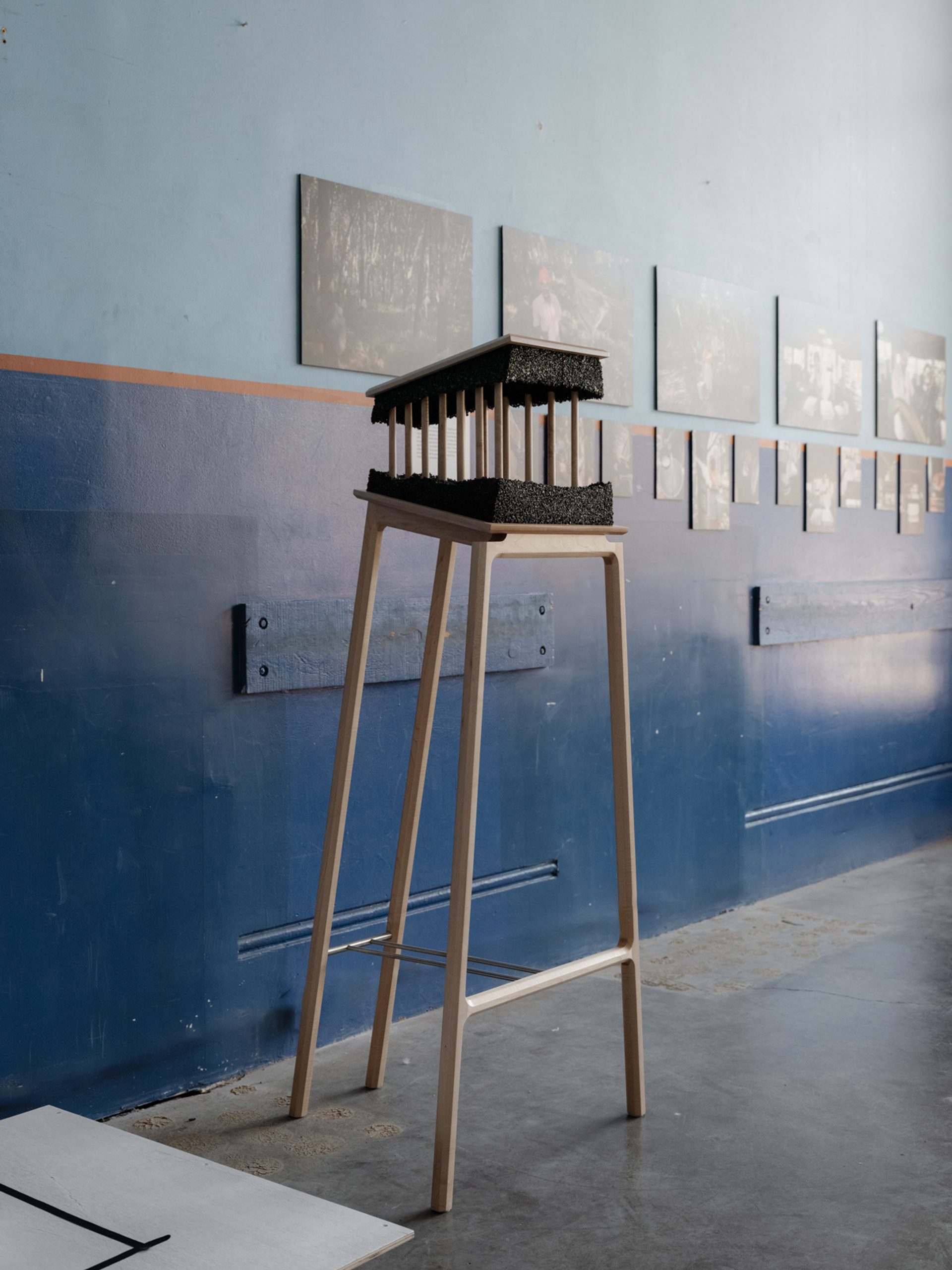 Tall legged table showcasing a 3d sculpture with photos on a wall in the background