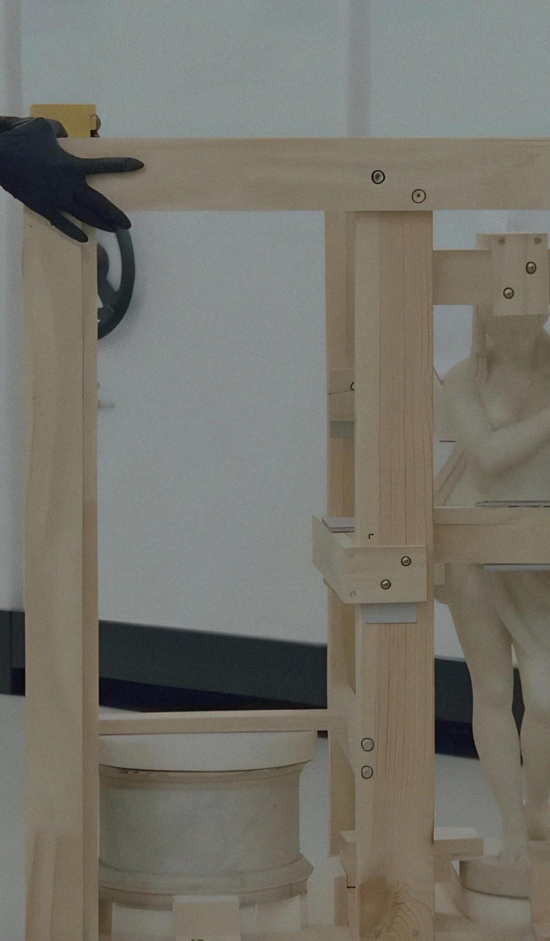 Two people packing a sculpture with secure wooden beams.