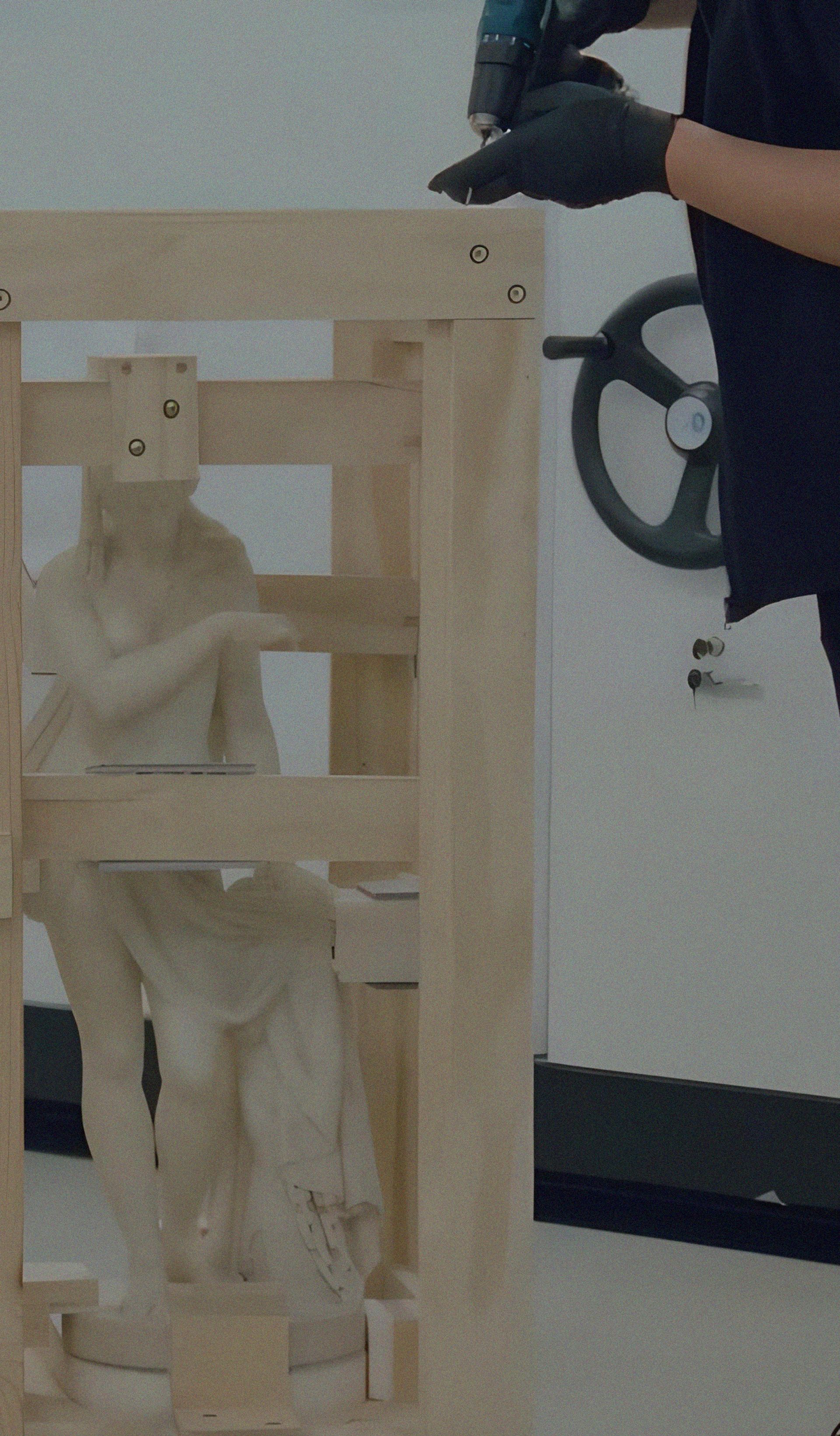 Two people packing a sculpture with secure wooden beams.