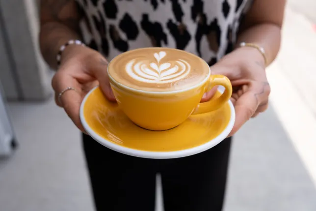 Frau hält gelbe Tasse mit Latte Art