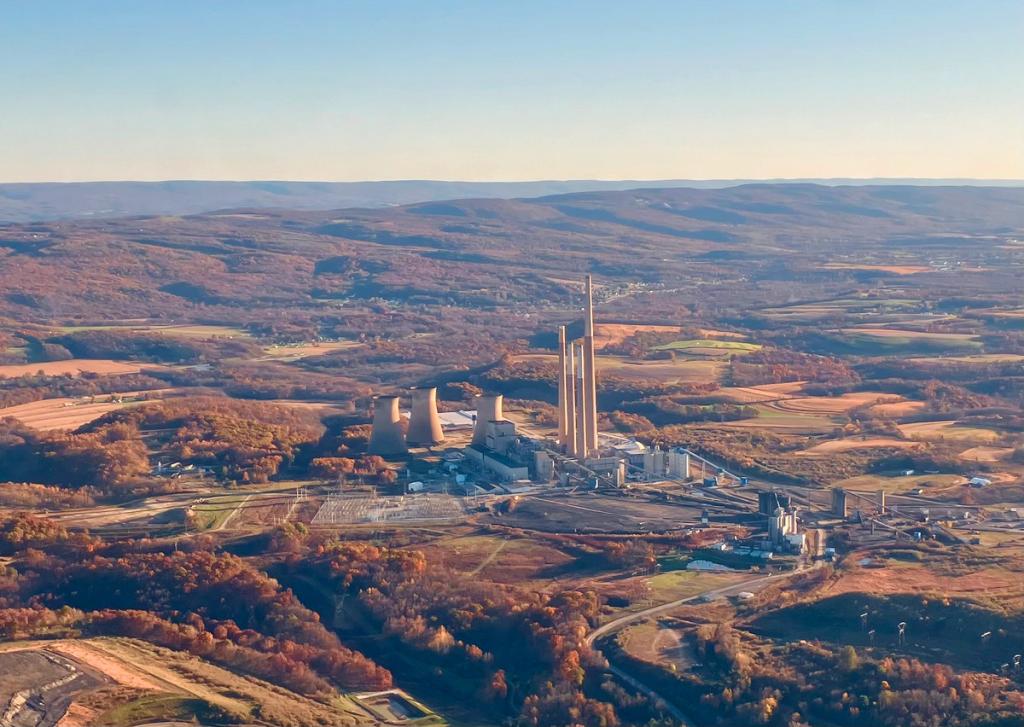 An aerial wide shot of a large industrial power plant with massive cooling towers and tall smokestacks, surrounded by rolling hills and rural landscape in autumn.