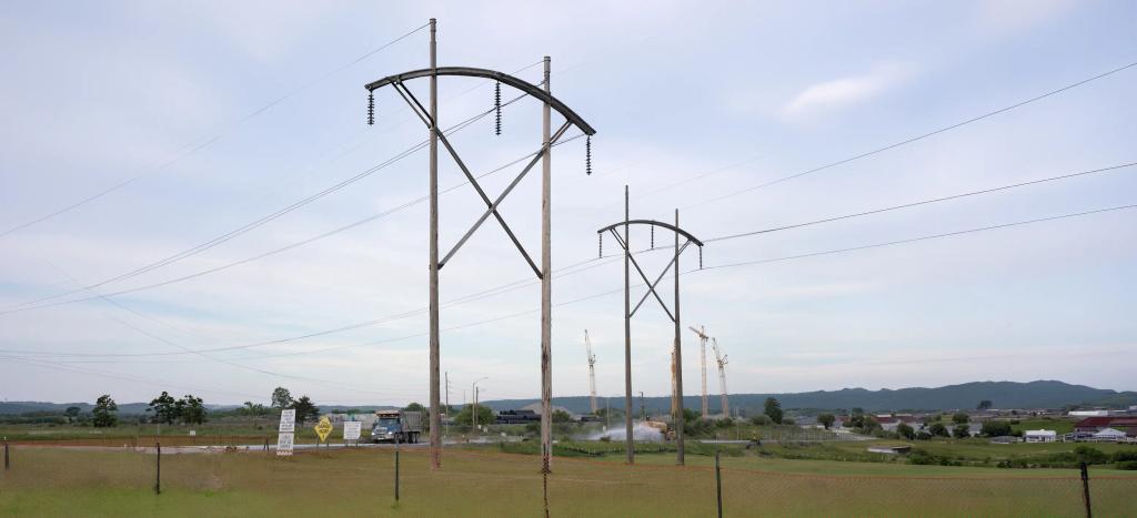 Transmission towers and power lines above the Homer City site, with construction cranes working in the distance.