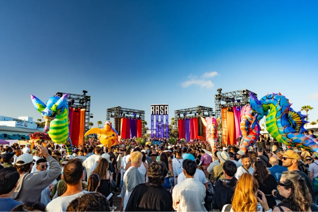 A festival crowd in front of the RASA stage, flanked by giant inflatable dragons under a blue sky.