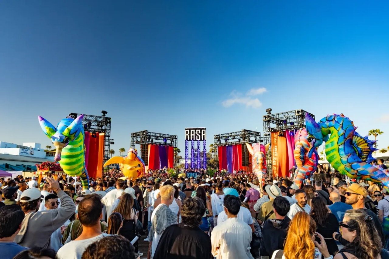 A festival crowd in front of the RASA stage, flanked by giant inflatable dragons under a blue sky.