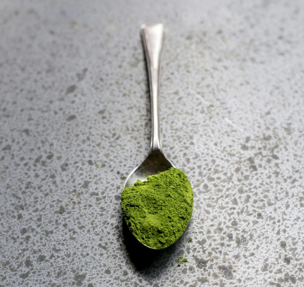 A spoonful of green powder on a speckled grey surface.
