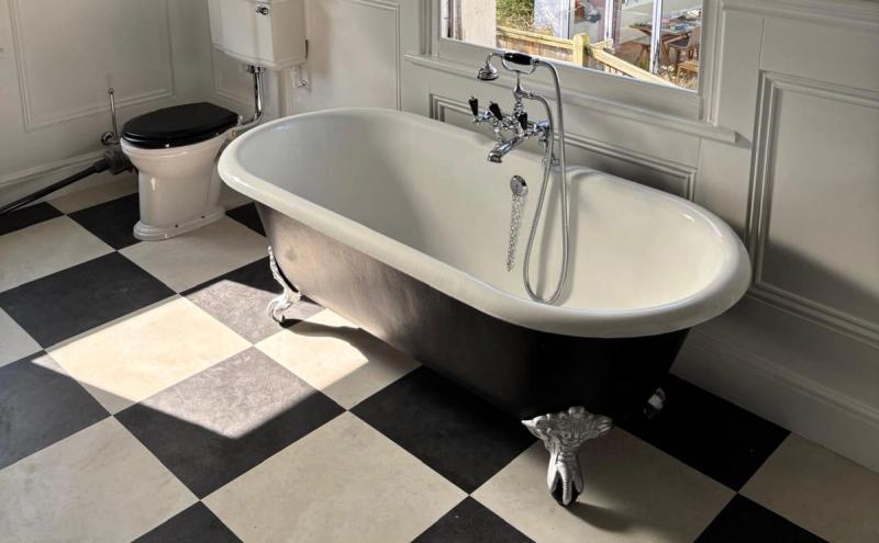 Clawfoot tub beneath window in green-tiled bathroom