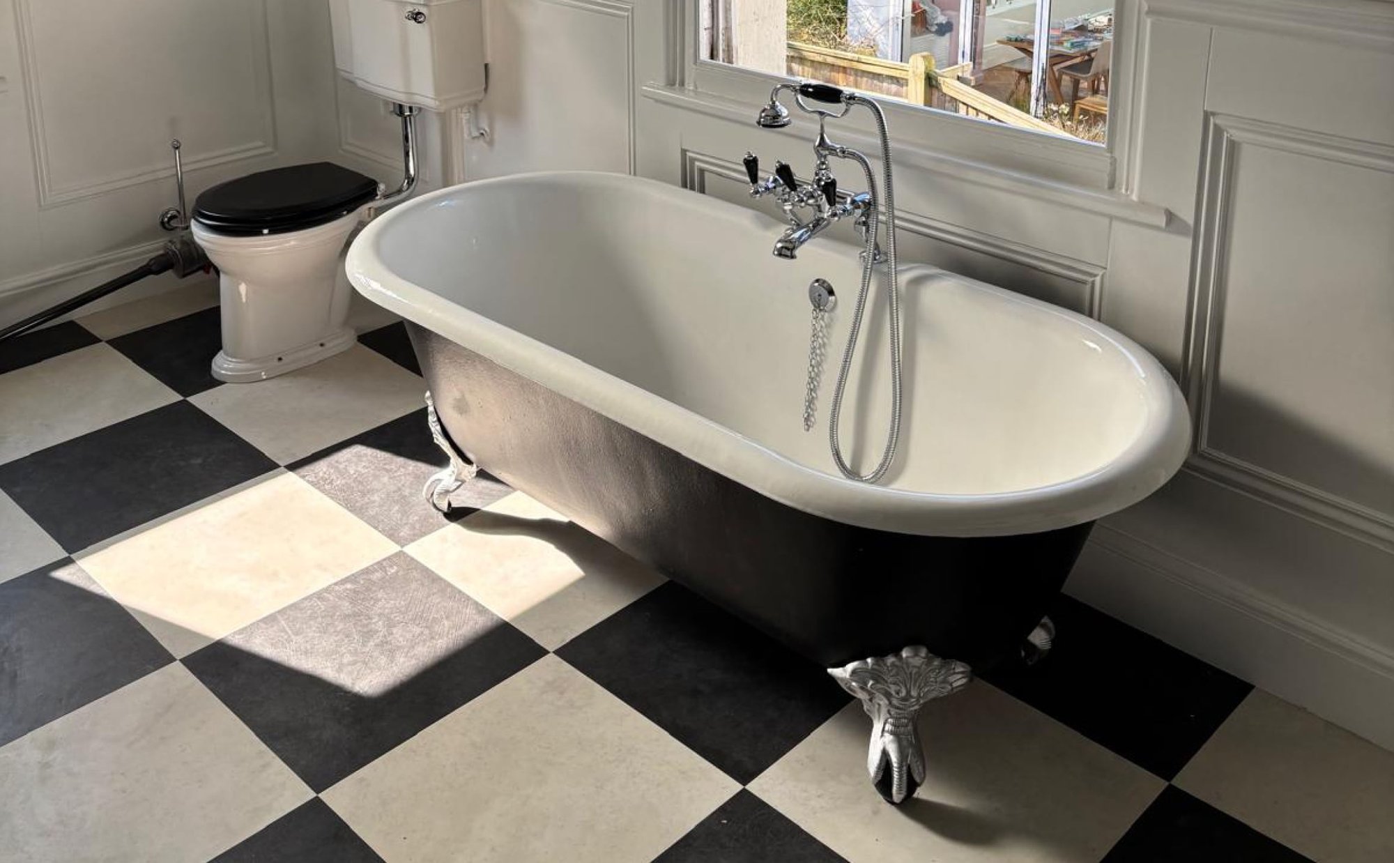 Clawfoot tub beneath window in green-tiled bathroom