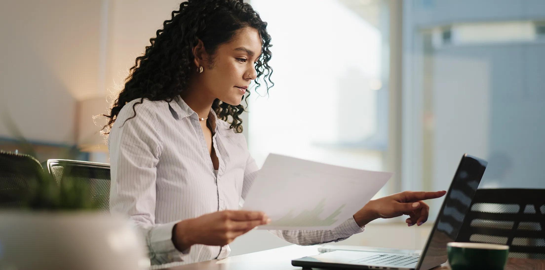 A professional comparing a printed report with information on a laptop.